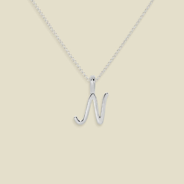 A silver initial necklace featuring a polished uppercase letter 'N' pendant on a delicate silver chain, set against a solid light beige background.