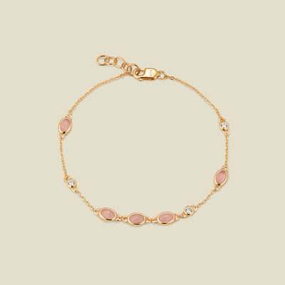 Gold bracelet with bezel-set pink and clear stones against a neutral background.