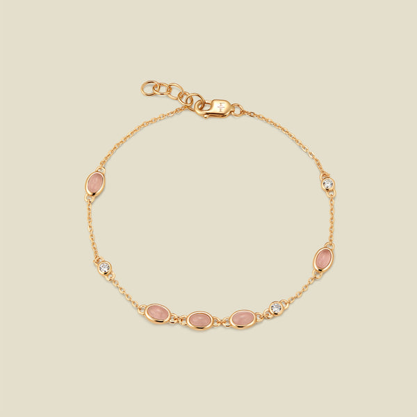 Gold bracelet with bezel-set pink and clear stones against a neutral background.