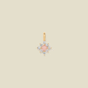 Gold charm with prong-set pink and clear stones against a neutral background.