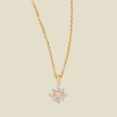 Gold chain with a pink prong-set pendant against a neutral backdrop.