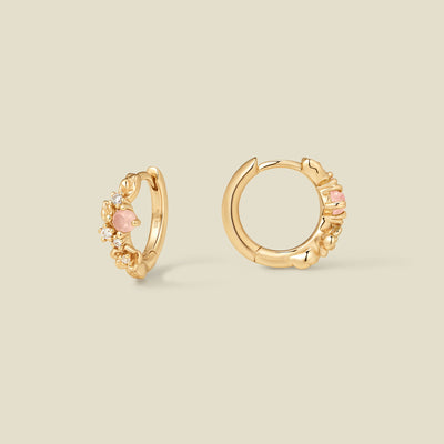 Gold hoop earrings with prong-set pink and clear stones against a neutral background.