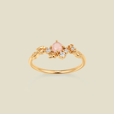 Gold ring with floral embellishments and pink and clear prong-set stones against a neutral background.