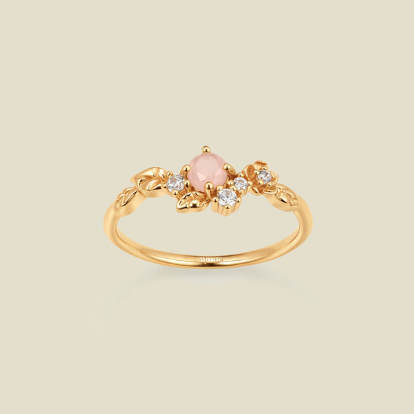 Gold ring with floral embellishments and pink and clear prong-set stones against a neutral background.