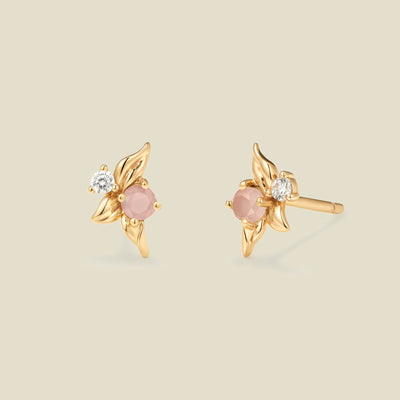 Gold stud earrings with prong set pink and clear stones against a neutral backdrop.