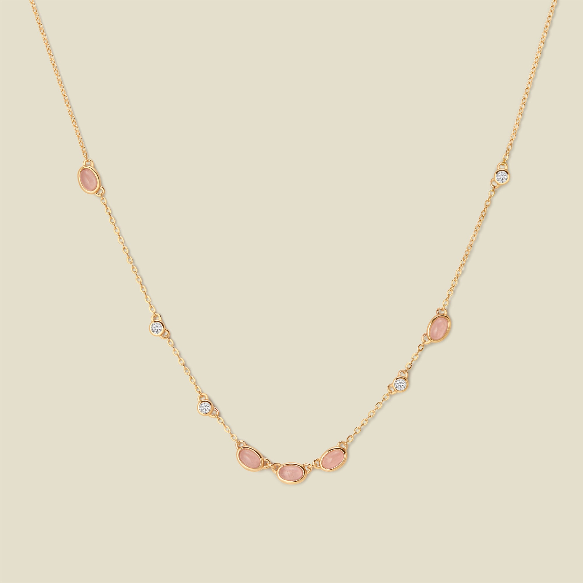 Gold necklace with pink and clear bezel-set stones against a neutral backdrop.