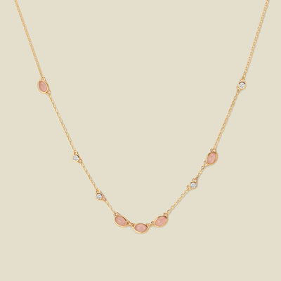 Gold necklace with pink and clear bezel-set stones against a neutral backdrop.