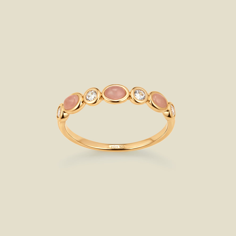 Gold ring with bezel-set pink and clear stones against a neutral background.