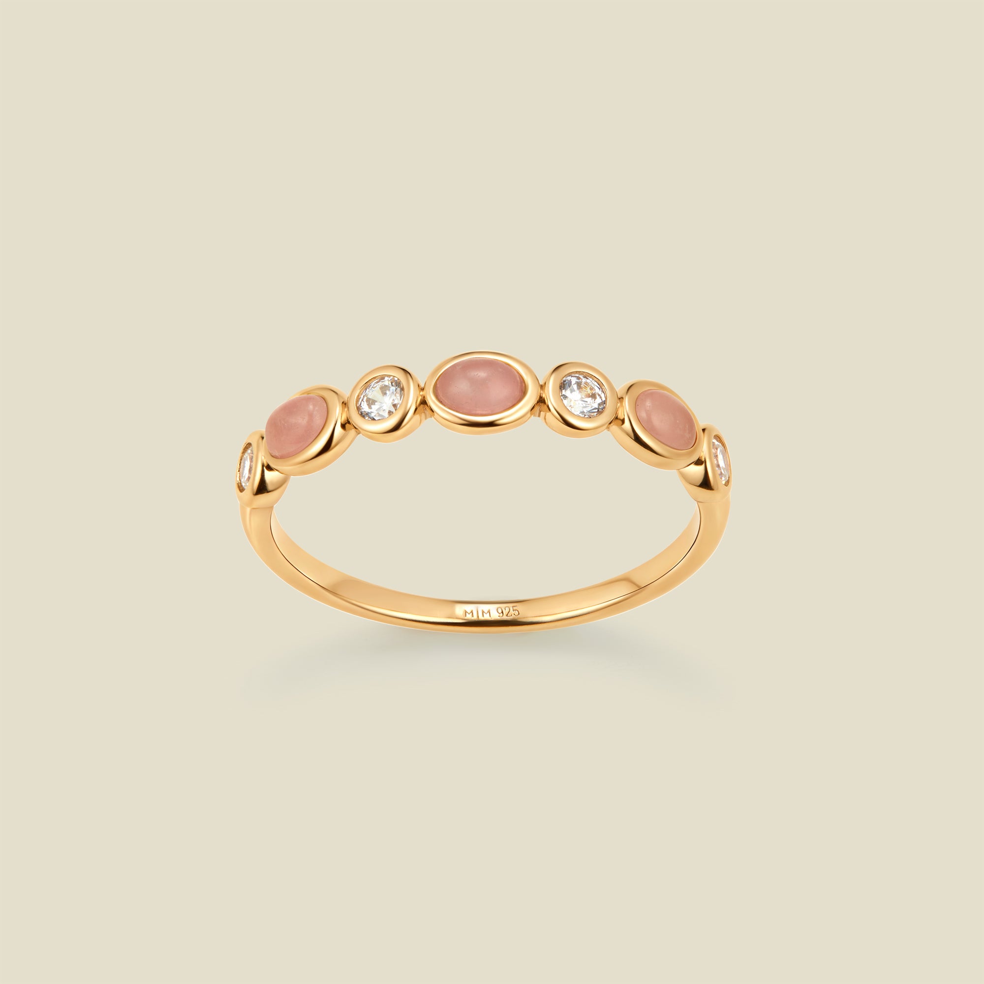 Gold ring with bezel-set pink and clear stones against a neutral background.
