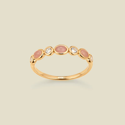 Gold ring with bezel-set pink and clear stones against a neutral background.
