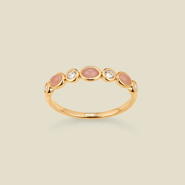 Gold ring with bezel-set pink and clear stones against a neutral background.