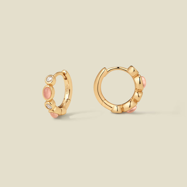 Pair of gold hoop earrings with pink and clear bezel set stones against a neutral background.