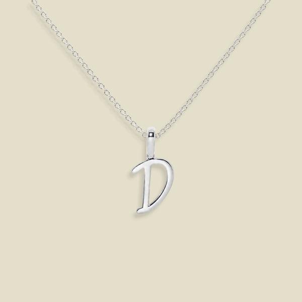 A silver initial necklace featuring a polished script font 'D' pendant on a delicate cable chain, set against a solid light beige background.