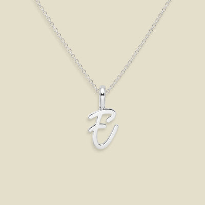 A silver initial necklace featuring a polished cursive letter 'E' pendant on a delicate cable chain, set against a solid light beige background.
