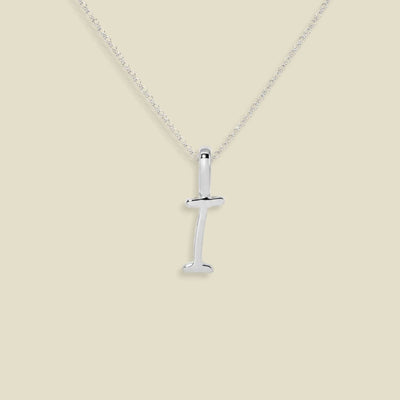 A silver initial necklace featuring a polished letter 'I' pendant in script font on a delicate silver chain, set against a solid light beige background.