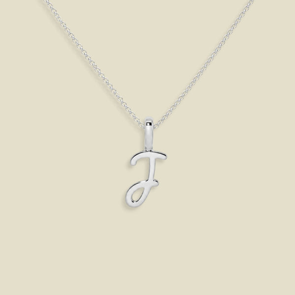 A silver initial pendant necklace featuring the uppercase letter 'J' in a cursive script, suspended from a delicate silver chain against a solid beige background.