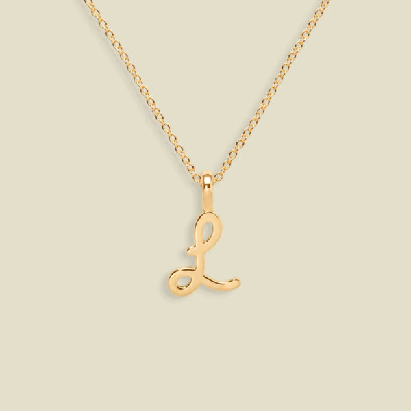 A dainty gold necklace with a polished gold cursive uppercase letter 'L' pendant, displayed against a solid light beige background.