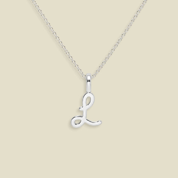 A silver initial necklace featuring a polished cursive letter 'L' pendant on a delicate link chain, set against a solid light beige background.