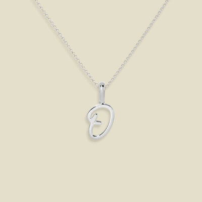 A silver initial pendant necklace featuring a script uppercase letter 'O' , suspended from a delicate silver chain against a solid light beige background.