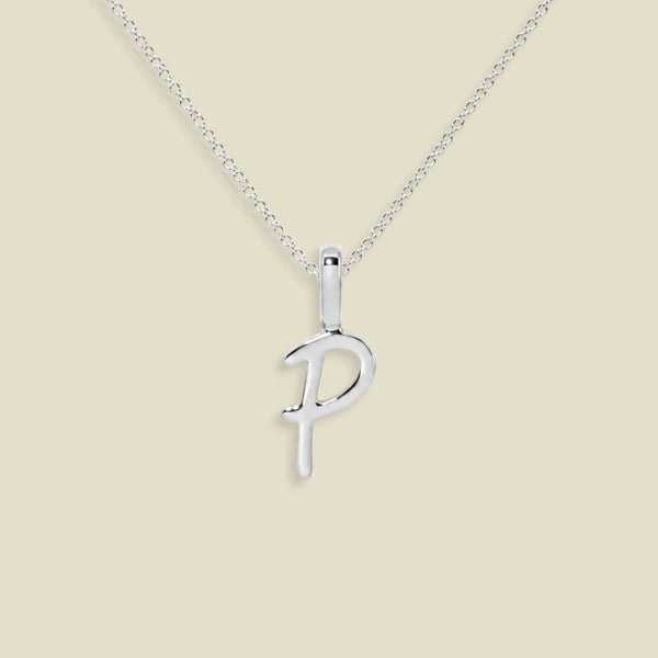 A silver initial pendant necklace featuring the uppercase letter 'P' on a delicate silver chain, set against a solid light beige background.