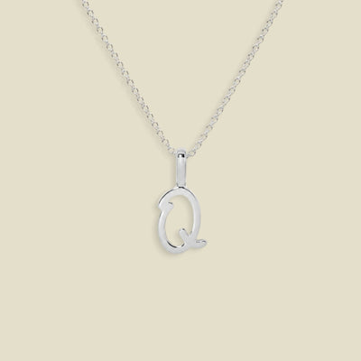 A silver initial necklace featuring a polished upperrcase 'Q' pendant on a delicate silver chain, set against a solid light beige background.