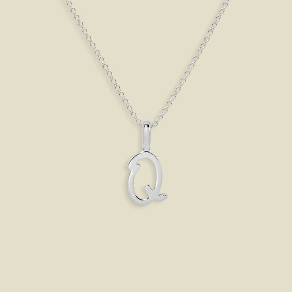 A silver initial necklace featuring a polished upperrcase 'Q' pendant on a delicate silver chain, set against a solid light beige background.