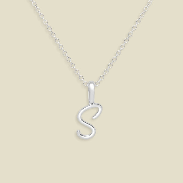A silver initial necklace featuring a polished cursive letter 'S' pendant on a delicate silver chain, set against a solid light beige background.