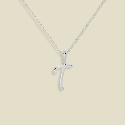 A silver initial pendant necklace featuring the uppercase letter 'T' on a delicate silver chain, set against a solid beige background.