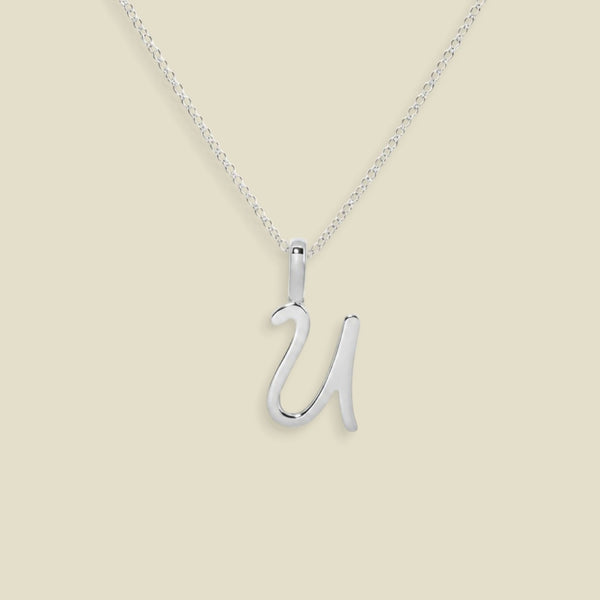 A silver initial necklace featuring an uppercase cursive letter 'U' pendant on a delicate silver chain, set against a solid light beige background.