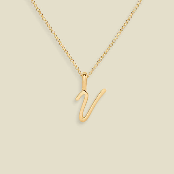A gold initial necklace featuring a polished uppercase script letter 'V' pendant on a delicate gold chain, set against a solid light beige background.
