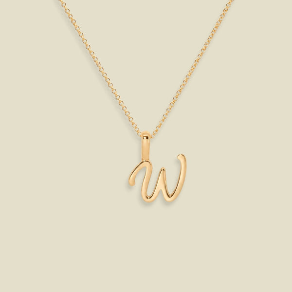 A gold initial necklace featuring a cursive uppercase script letter 'W' pendant on a delicate gold chain, set against a solid light beige background.