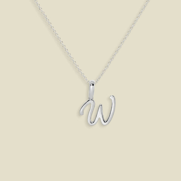 A silver initial necklace featuring a polished cursive uppercase letter 'W' pendant on a delicate silver chain, set against a solid light beige background.