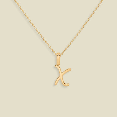 A gold initial necklace featuring a polished uppercase-style letter 'X' pendant on a delicate gold chain, set against a solid light beige background.
