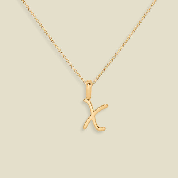 A gold initial necklace featuring a polished uppercase-style letter 'X' pendant on a delicate gold chain, set against a solid light beige background.