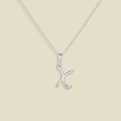 A silver initial necklace featuring a polished cursive uppercase letter 'X' pendant on a delicate link chain, set against a solid light beige background.