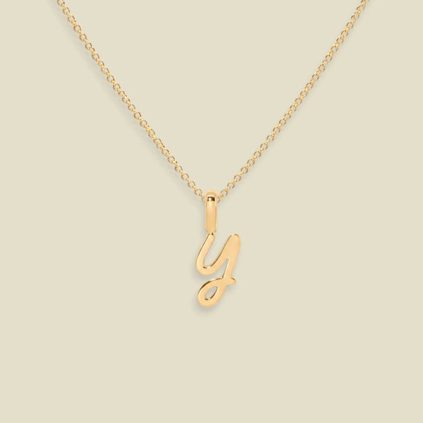 A delicate gold chain necklace featuring a polished cursive letter 'Y' pendant, displayed against a solid light beige background.