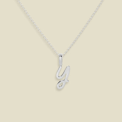 A silver initial necklace featuring a polished cursive letter 'Y' pendant on a delicate silver cable chain, set against a solid light beige background.