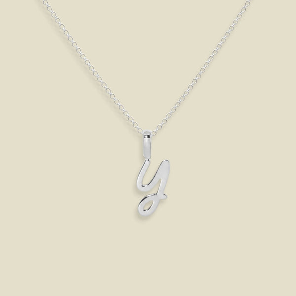 A silver initial necklace featuring a polished cursive letter 'Y' pendant on a delicate silver cable chain, set against a solid light beige background.