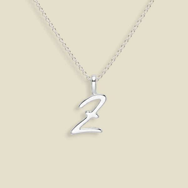 A silver initial necklace featuring a polished cursive letter 'Z' pendant on a delicate silver chain, set against a solid light beige background.