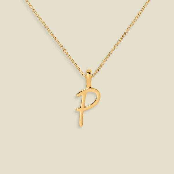 A gold initial necklace featuring a cursive uppercase-style letter 'P' pendant on a delicate gold chain, set against a solid light beige background.