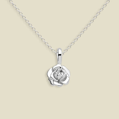 A silver peony pendant necklace on a delicate silver chain, set against a solid light beige background.