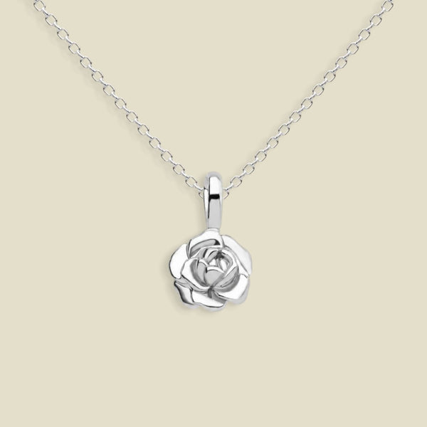 A silver peony pendant necklace on a delicate silver chain, set against a solid light beige background.