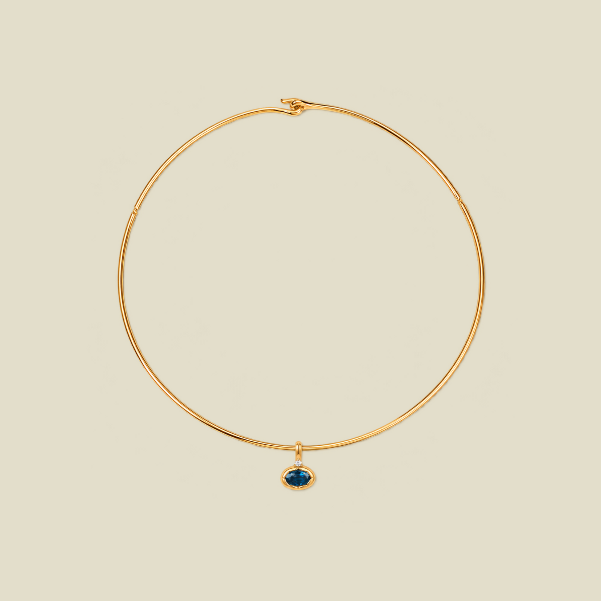 A thin gold wire hoop necklace with a small oval blue-green gemstone pendant, displayed on a solid light beige background.
