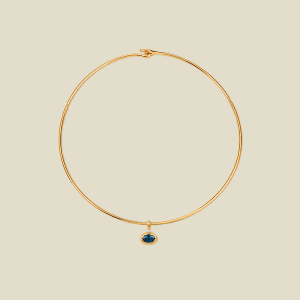 A thin gold wire hoop necklace with a small oval blue-green gemstone pendant, displayed on a solid light beige background.