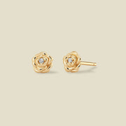 A pair of gold peony stud earrings, one shown from the front and the other from the side, each featuring a small clear gemstone at the center, set against a solid light beige background.
