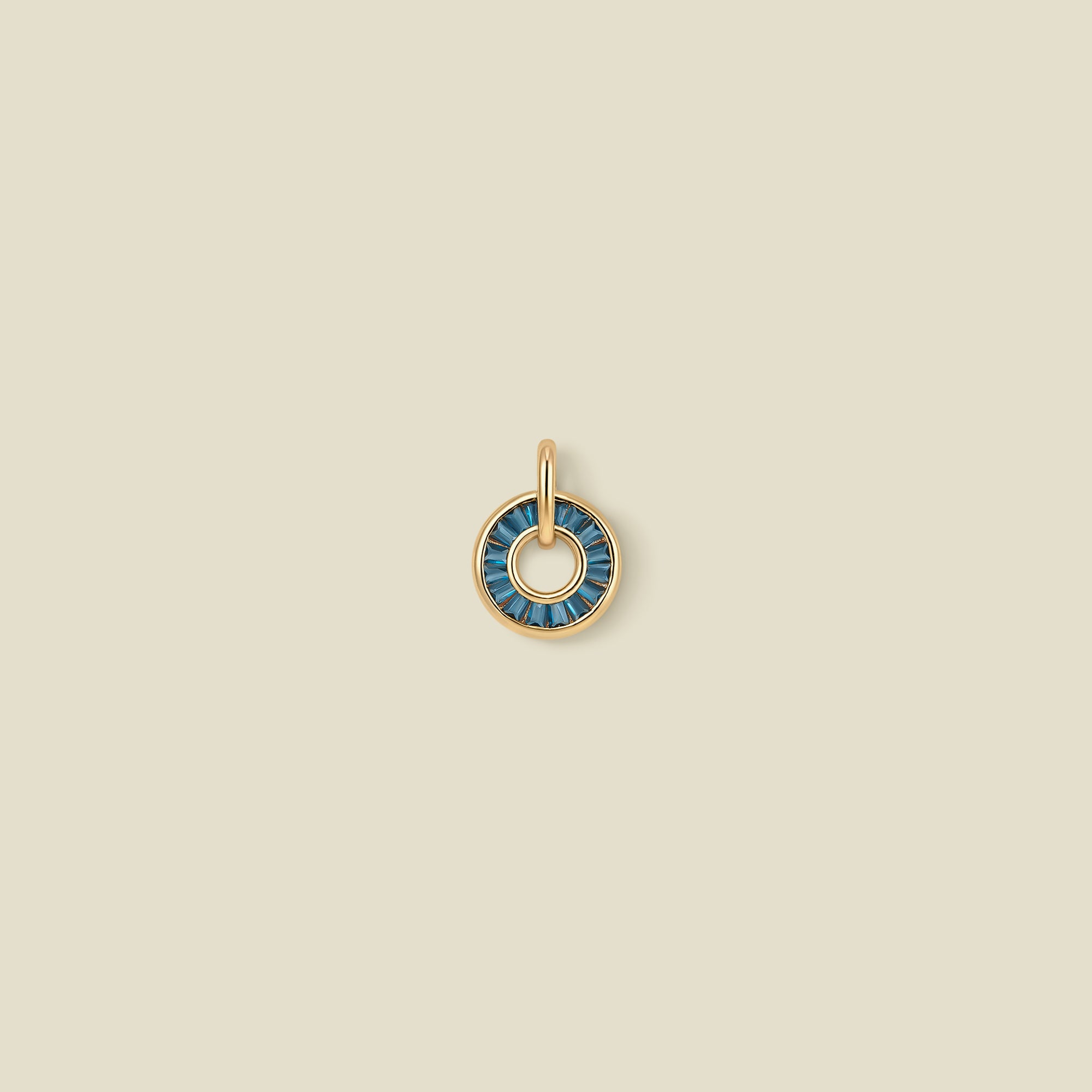 A gold circular pendant featuring blue-green baguette-cut stones around a hollow center, displayed against a solid light beige background.