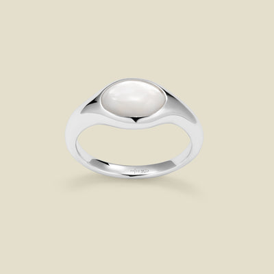 Silver ring with a bezel-set pearl stone against a neutral background.