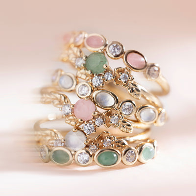 Six gold hoop earrings with pink, green and white stones stacked on top of each other