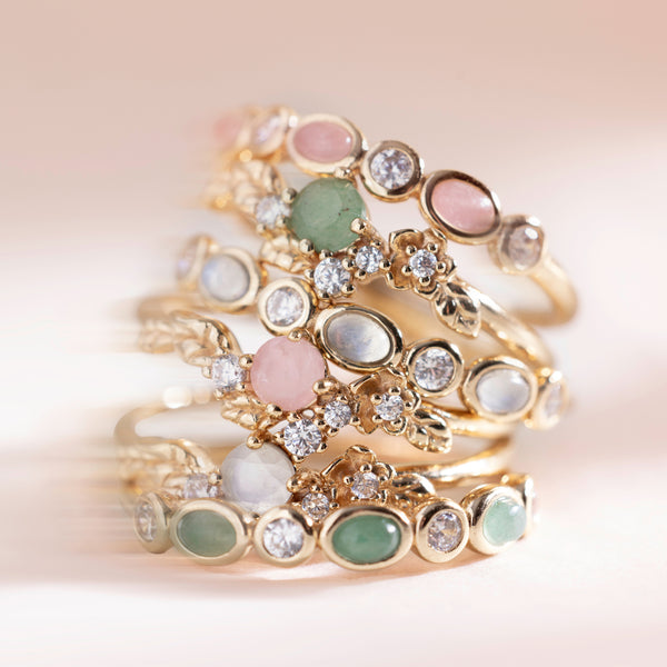 Six gold hoop earrings with pink, green and white stones stacked on top of each other