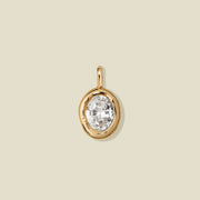 A large gold bezel-set clear oval gemstone, set against a solid beige background.